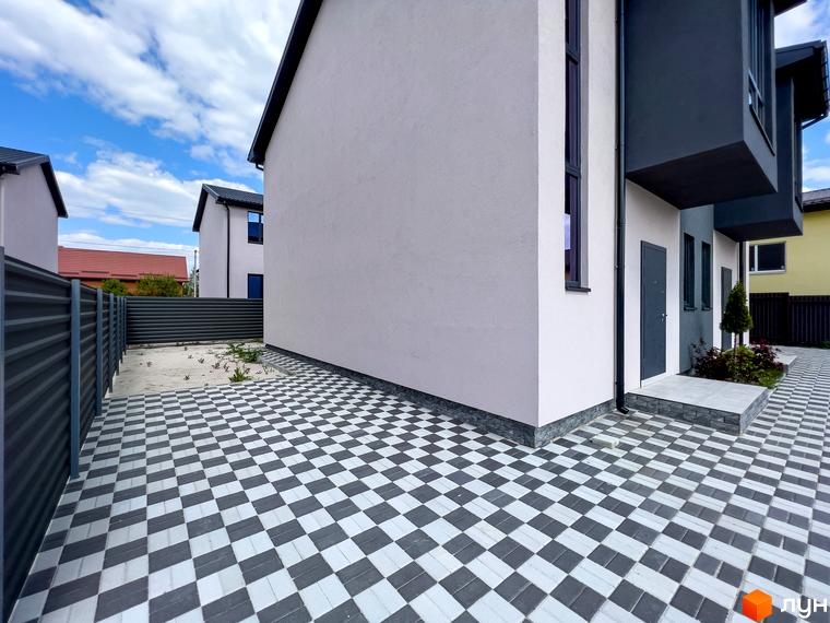 Кутовий фасад будинку Котеджного містечка Одеський з світлими стінами та темними вікнами. Територія вимощена чорно-білою плиткою.