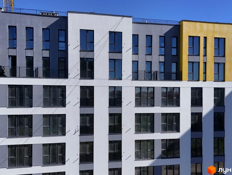 Фасад житлового комплексу Весняний з вікнами та балконами. Будинок має сірі, білі та жовті секції.
