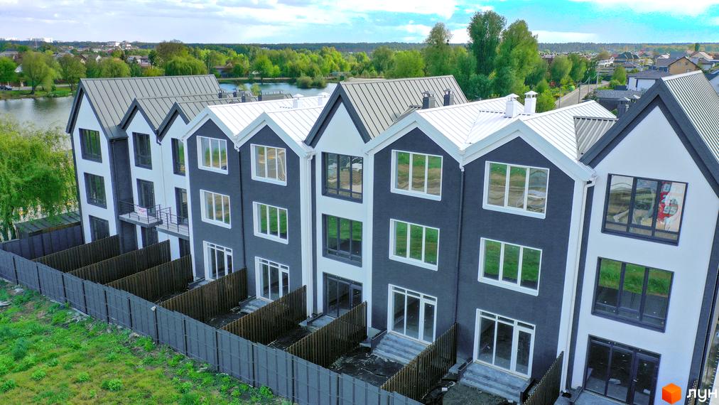 Зображення сторінки житлового комплексу таунхаус New Smart 15. Триповерхові будинки з темними фасадами, білими вікнами та дахами, перед будинками паркан та газон.