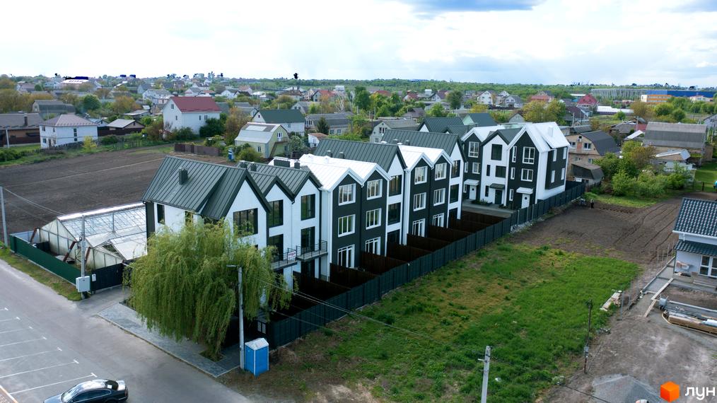 Зображення сторінки житлового комплексу New Smart 15. Будинки з білими та чорними фасадами, сірими дахами, огороджені парканом, поруч зелена зона та асфальтована дорога.