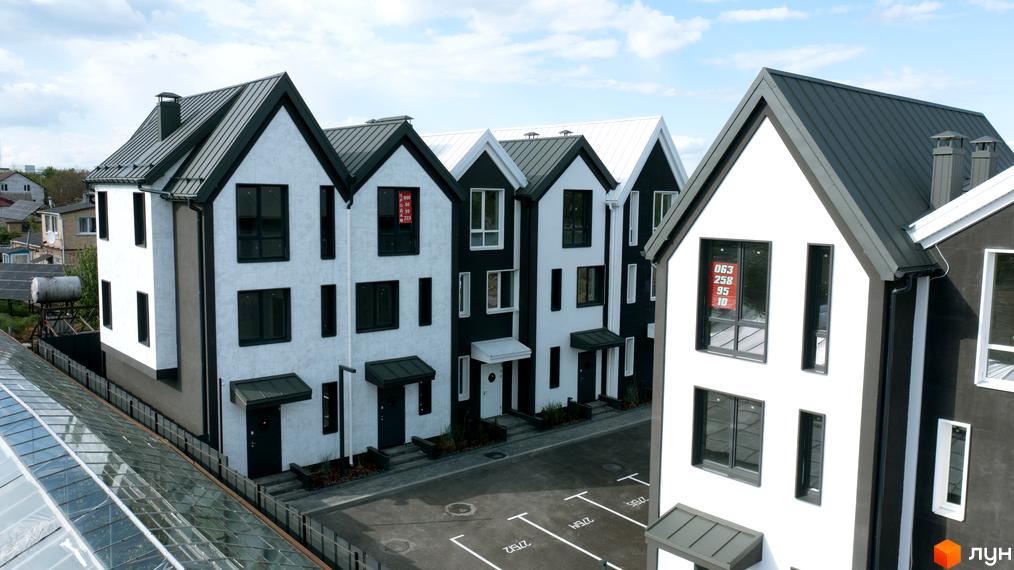 Зображення будинку житлового комплексу New Smart 15 з білими стінами та темним дахом. Перед будинком розташована парковка з розміткою.