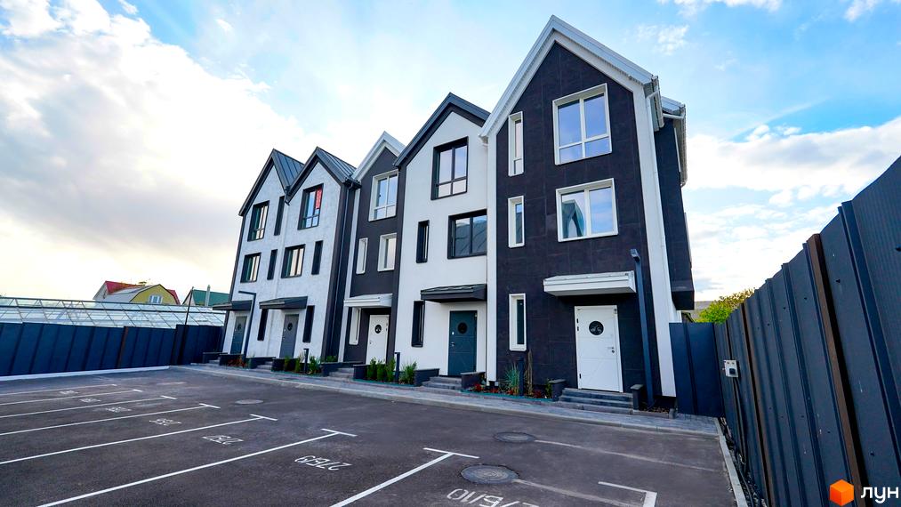 Зовнішній вигляд таунхаусів New Smart 15 з темним фасадом та білими вставками. Перед будинками розташована парковка.