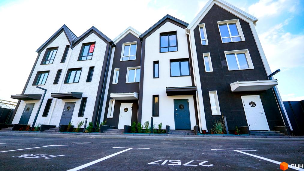 Зображення сторінки житлового комплексу. Таунхауси New Smart 15 з білими та темно-сірими фасадами, вхідними дверима та парковкою.