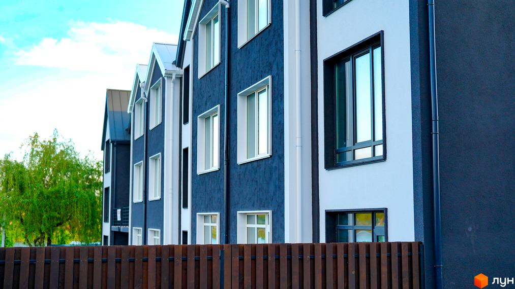 Таунхаус New Smart 15 з темно-синім фасадом та білими вікнами, огороджений дерев'яним парканом.