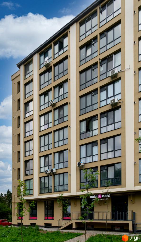 Фасад житлового комплексу на вул. Короля Данила, 11 бежевий, з темними вікнами, білими вставками та комерційними приміщеннями. Навколо будинку є зелені насадження.