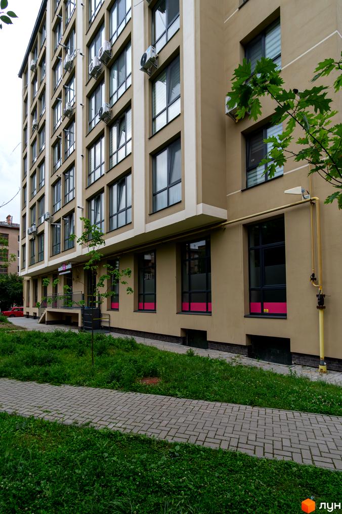 Багатоповерховий будинок nobi + nobi на вул. Короля Данила, 11 з бежевим фасадом та великими вікнами. Поруч розташовані зелені насадження та тротуарна доріжка.