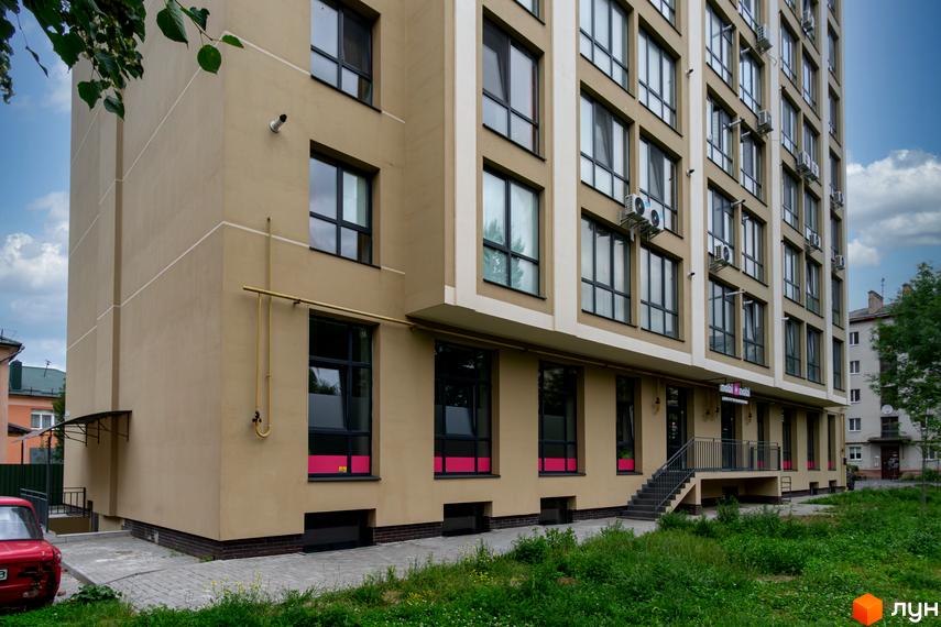 Фасад новобудови по вул. Короля Данила, 11, з великими темними вікнами та бежевими стінами. Поруч розташована прибудинкова територія з травою та доріжками.