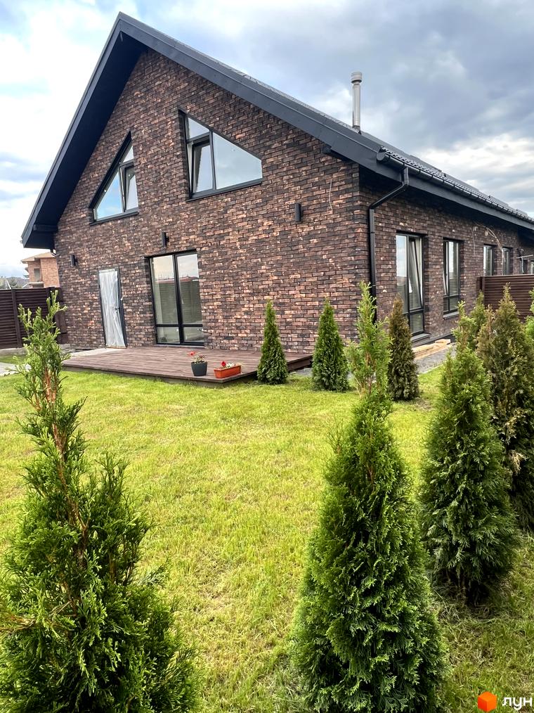 Зовнішній вигляд будинку з цегли у Котеджному містечку Одноповерховий Київ - Віта Поштова. Навколо будинку зелений газон та висаджені туї.