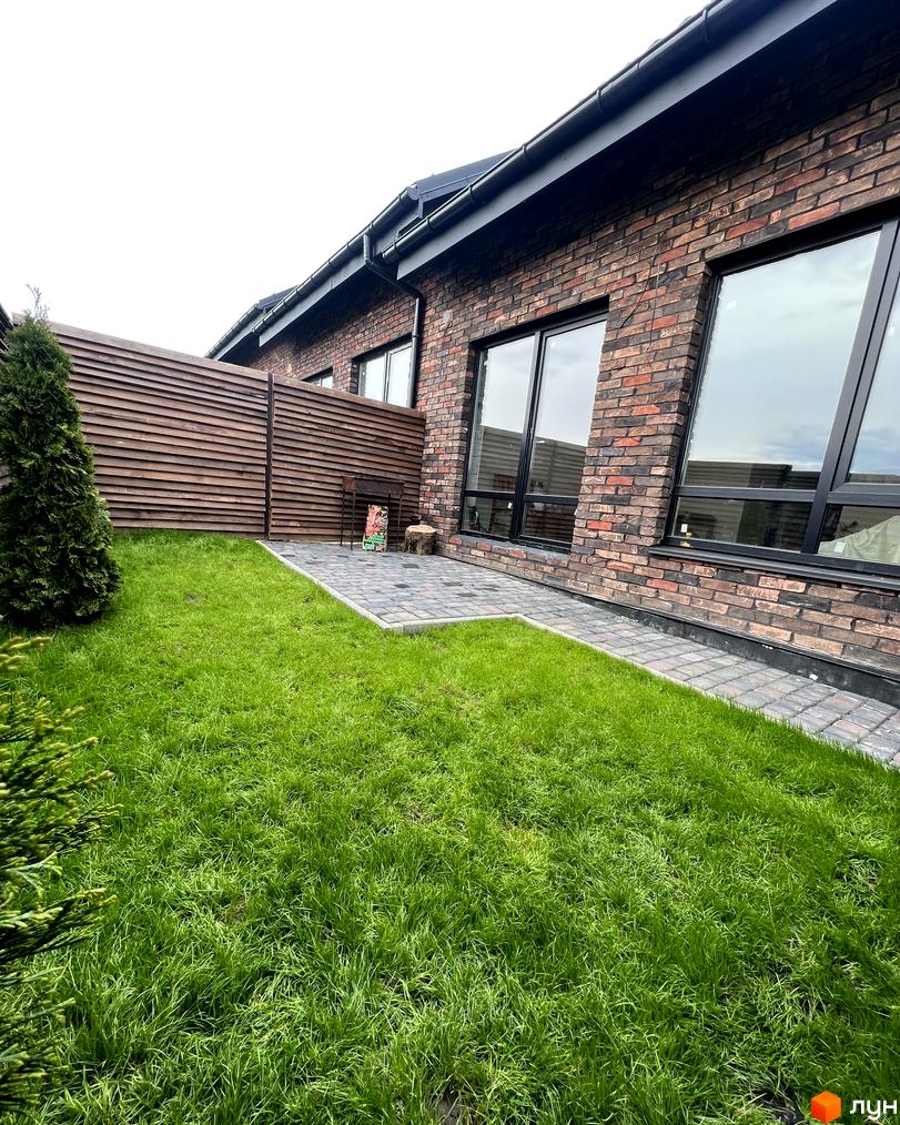 Вигляд цегляного будинку в Котеджному містечку Одноповерховий Київ - Віта Поштова з зеленим газоном та дерев'яною огорожею.