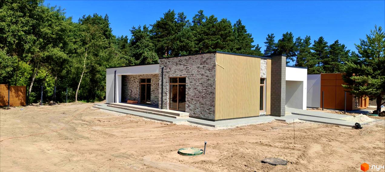 Котеджне містечко LOTUS: фасад будинку з цегли та дерев'яних панелей, прибудинкова територія з піщаним покриттям та зеленими насадженнями.