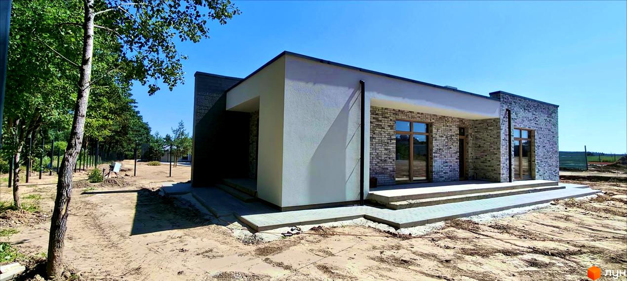 Котеджне містечко LOTUS: одноповерховий будинок з цегляним фасадом та білими стінами, розташований на піщаній ділянці з деревами.