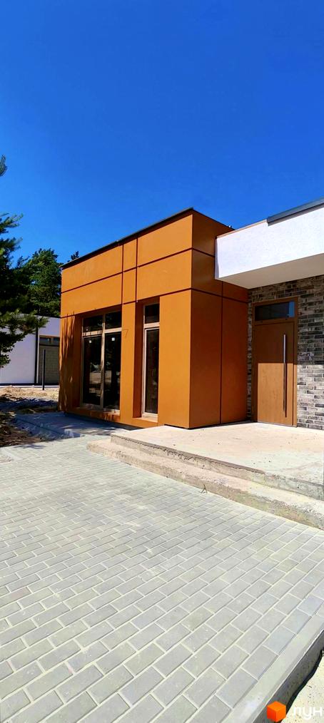 Котеджне містечко LOTUS: сучасна одноповерхова будівля з великими вікнами та цегляним фасадом, розташована на вимощеній плиткою території.