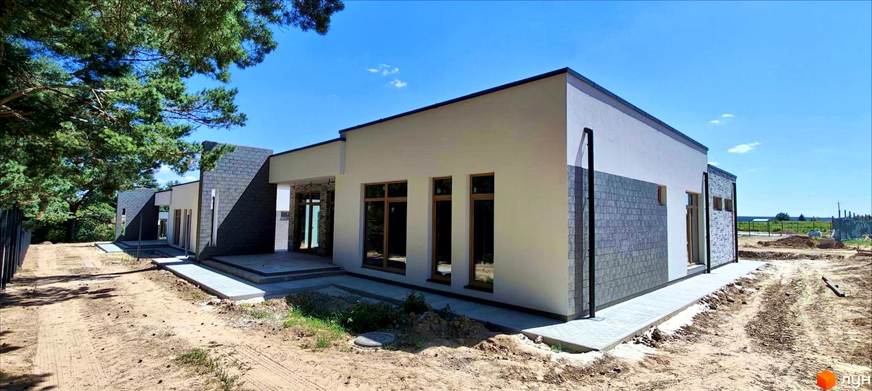 Котеджне містечко LOTUS: одноповерхові будинки з панорамними вікнами та сірим оздобленням фасаду, розташовані на ділянці з піщаним покриттям та зеленими насадженнями.