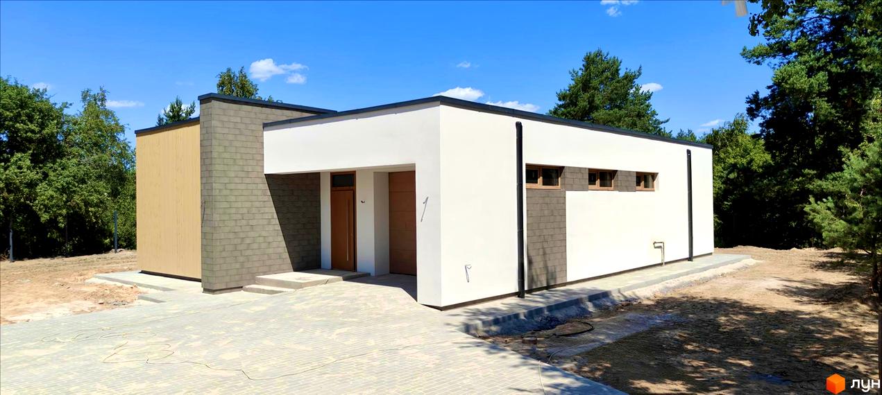 Котеджне містечко LOTUS: одноповерховий будинок з білою штукатуркою, дерев'яними елементами та сірою плиткою, розташований на бруківці біля зелених дерев.