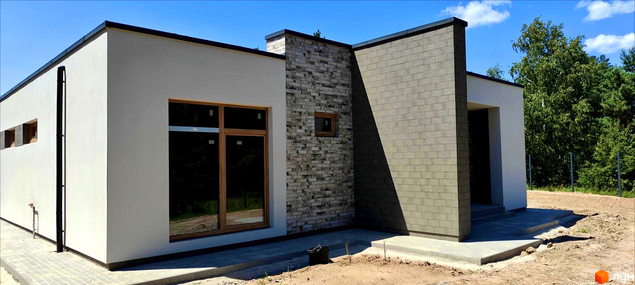 Зовнішній вигляд будинку КМ LOTUS з білою штукатуркою та сірою цегляною обробкою, прибудинкова територія з бруківкою та зеленими насадженнями.