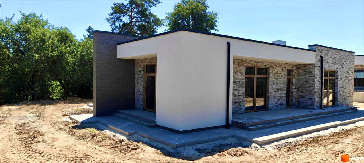 Котеджне містечко LOTUS: одноповерховий будинок з цегляним та білим фасадом, великими вікнами та сходами на тлі зелених дерев та блакитного неба.