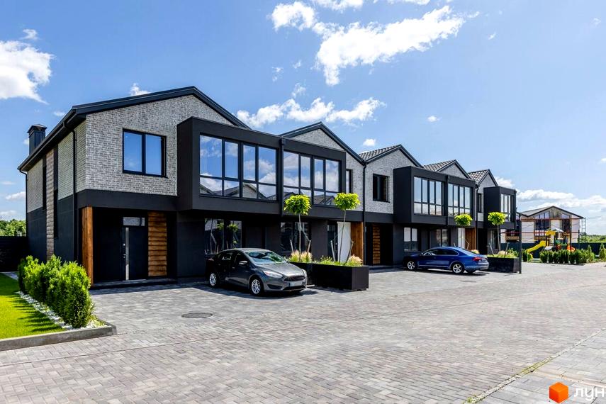 Котеджне містечко Romankiv Village. Сучасні таунхауси з великими вікнами та сірим цегляним фасадом, перед якими розташований вимощений сірою плиткою двір з автомобілями та зеленою зоною.