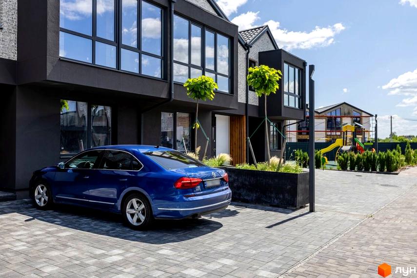 Котеджне містечко Romankiv Village: фасади будинків з великими вікнами, синій автомобіль на бруківці, дитячий майданчик на території.