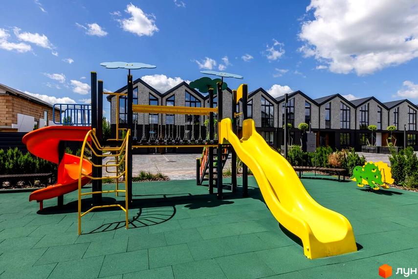 Дитячий майданчик з гірками та гойдалками на фоні котеджного містечка КМ Romankiv Village. Сучасні будинки з панорамними вікнами.