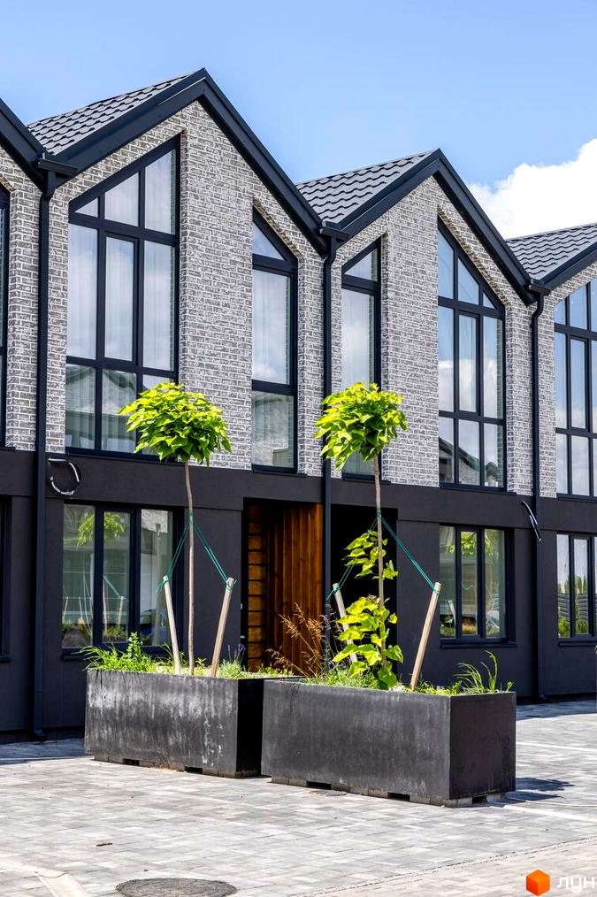 Котеджне містечко Romankiv Village: фасади будинків з сірої цегли та великими вікнами, прибудинкова територія з рослинами у великих бетонних клумбах.