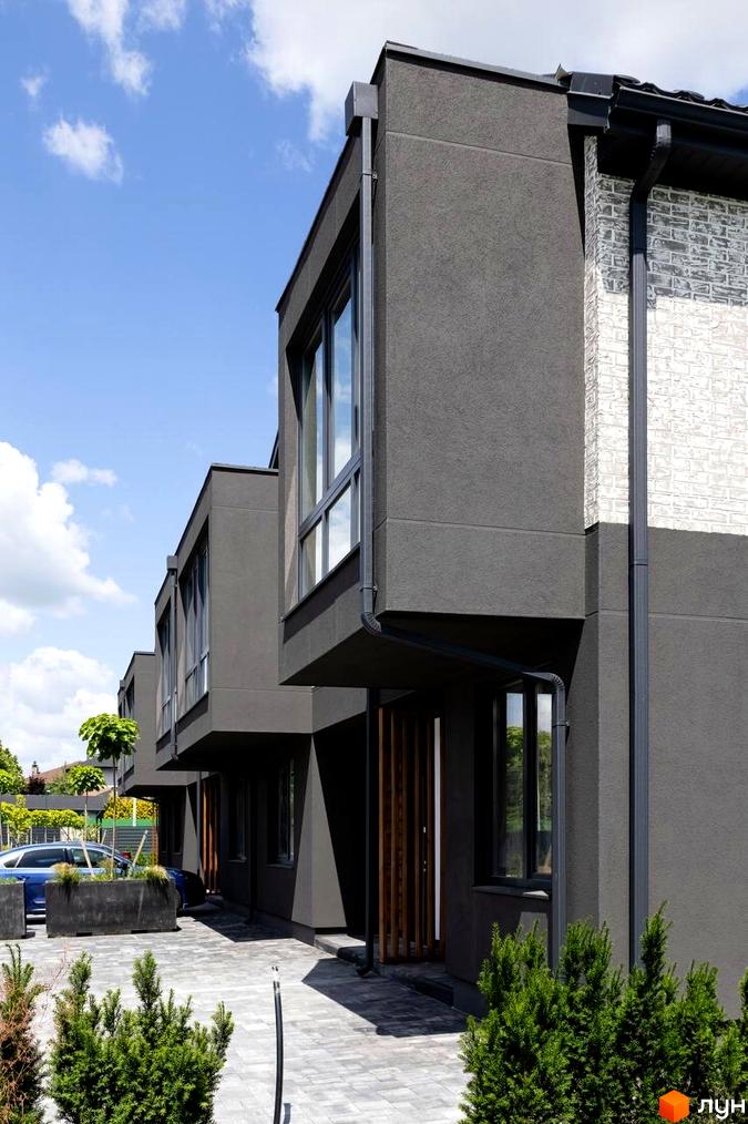 Котеджне містечко Romankiv Village. Зовнішній вигляд будинків з сірим фасадом та білою цегляною кладкою, прибудинкова територія з бруківкою та зеленими насадженнями.