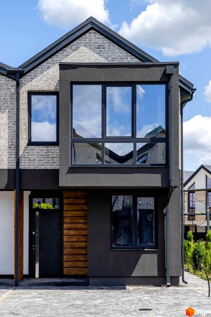Зовнішній вигляд будинку в котеджному містечку КМ Romankiv Village з сірої цегли та темною штукатуркою, великими вікнами та дерев'яними елементами. На прибудинковій території видно бруківку та зелені насадження.