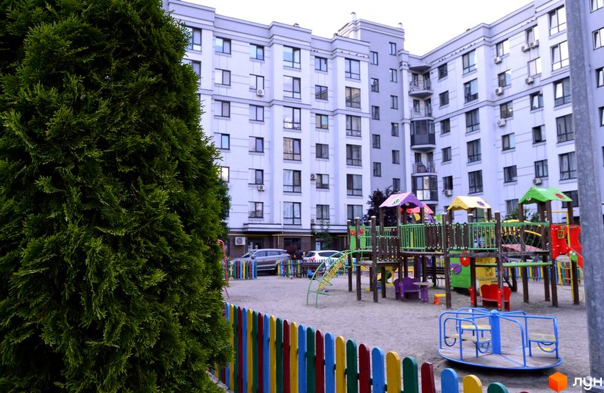 Житловий комплекс Новий Хотів з дитячим майданчиком та паркуванням біля будинку. Зовнішній вигляд новобудови з багатьма вікнами та балконами.