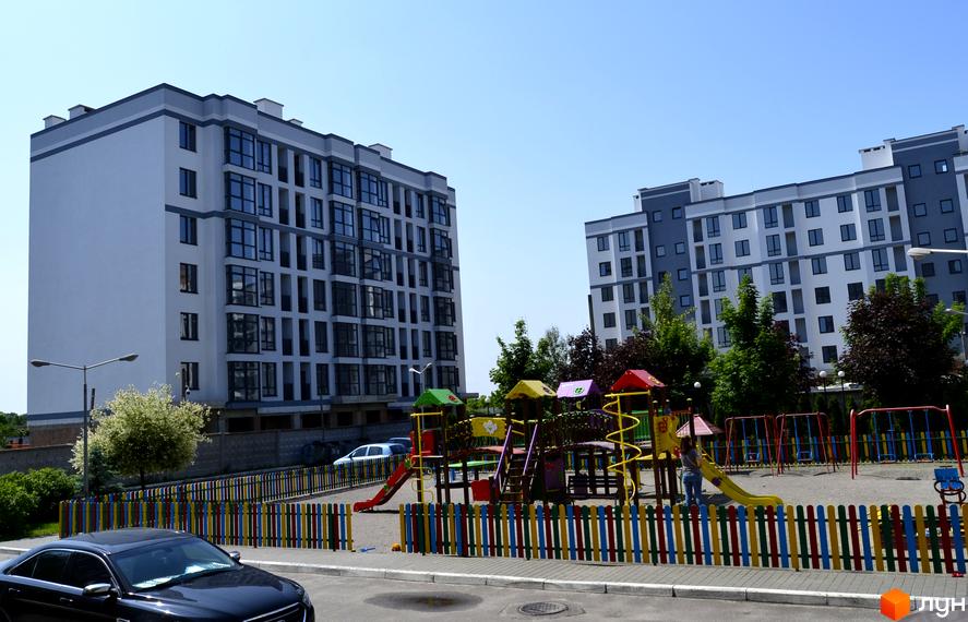 Новобудова ЖК Новий Хотів з сучасним фасадом та дитячим майданчиком на прибудинковій території. Комплекс має багатоповерхові будинки з великими вікнами.
