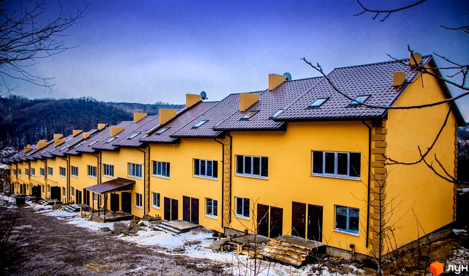 Житловий комплекс на вулиці Київська, 128. Зовнішній вигляд жовтих будинків з коричневими дахами, вікнами та дверима. Навколо будинків видно сніг та гілки дерев.