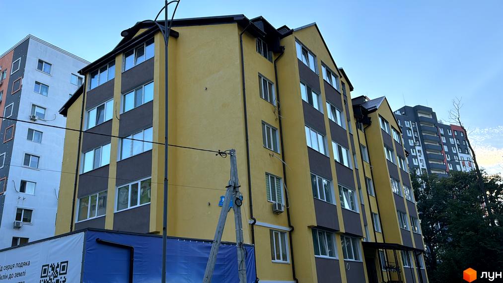 Зовнішній вигляд новобудови ЖК Академквартал-3 з жовто-сірим фасадом та численними вікнами. На передньому плані видно частину будівельного проєкту.