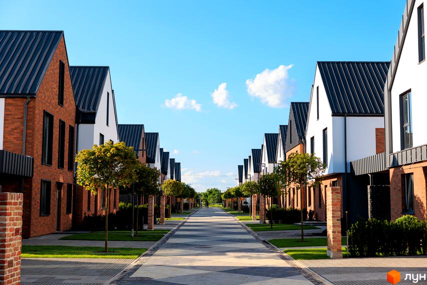 Котеджне містечко LAGOM з цегляними та білими фасадами будинків та акуратними деревами вздовж алеї. Фотографія новобудови.