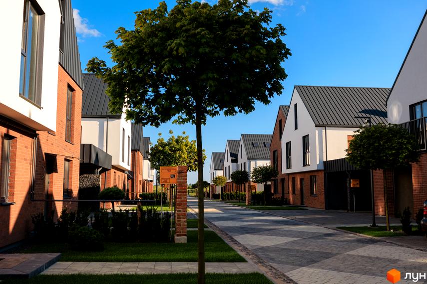 Котеджне містечко LAGOM: фасади будинків з червоної цегли та білої штукатурки, сірі дахи, зелена прибудинкова територія з деревами.