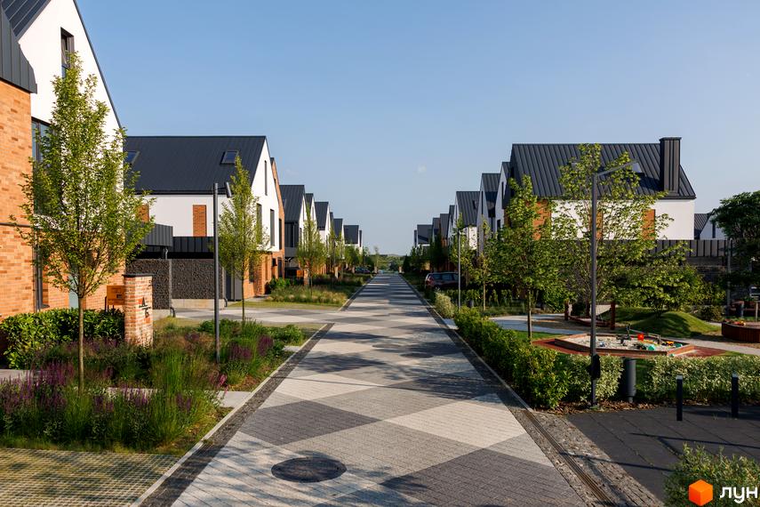 Котеджне містечко LAGOM: ряд білих будинків з темними дахами та доглянутою територією з алеєю та дитячим майданчиком.