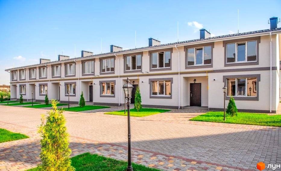 Котеджне містечко Паларіс: фасади двоповерхових будинків світло-сірого кольору з сірими віконними рамами, зелені газони та бруківка на території.