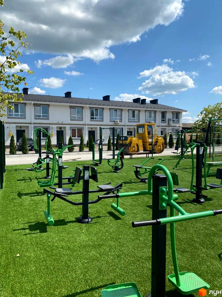 Зовнішній вигляд будинків житлового комплексу КМ Palaris з прибудинковою територією, що включає спортивні тренажери та зелене покриття.
