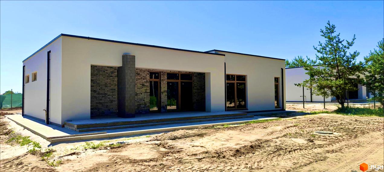 Котеджне містечко LOTUS: фасад будинку з цегляними елементами та великими вікнами, прибудинкова територія з піщаним покриттям та зеленими насадженнями.