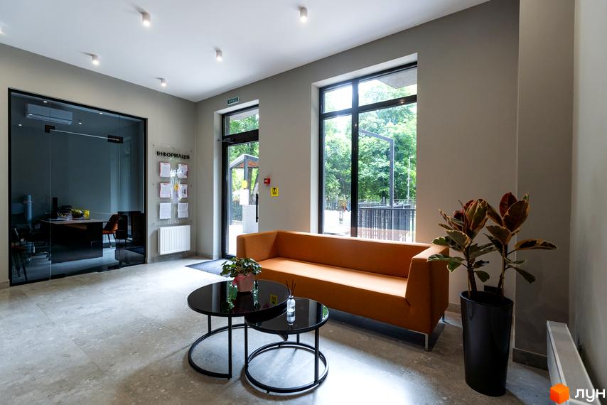 Апарт-комплекс Ітака: рецепція з диваном та журнальними столиками, скляними дверима та великими вікнами з видом на зелень.