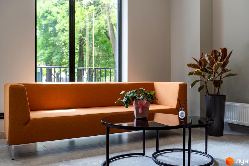 Апарт-комплекс Ітака: затишна зона відпочинку з помаранчевим диваном біля великого вікна з видом на зелень. Сучасний інтер'єр для комфортного життя.
