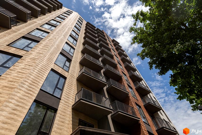 Апарт-комплекс Ітака з цегляним фасадом та балконами на фоні блакитного неба з хмарами. Будинок має багато вікон та виступаючі балкони.