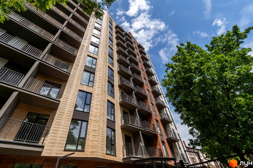 Апарт-комплекс Ітака з цегляним фасадом та балконами, розташований біля зелених дерев під блакитним небом.