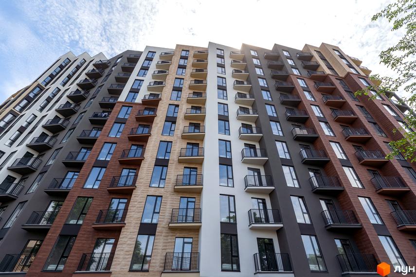 Апарт-комплекс Ітака - фасади будівлі з балконами та вікнами, виконані в різних кольорах: білому, сірому, коричневому та пісочному. Вид знизу на багатоповерховий будинок.