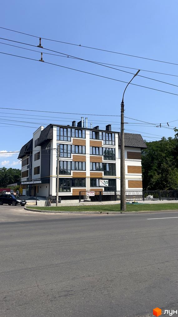 Житловий комплекс Соснівський затишок – це 5-поверхова новобудова з панорамними вікнами та дерев'яними вставками, розташована біля дороги з зеленою прибудинковою територією.