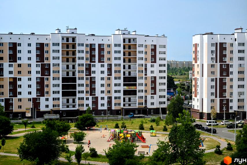 Житловий комплекс Сади Вишневі: багатоповерхові будинки з біло-коричневим фасадом та дитячим майданчиком на прибудинковій території.