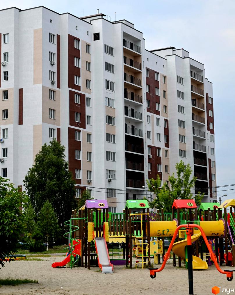 Житловий комплекс Сади Вишневі: багатоповерховий будинок з балконами та дитячим майданчиком на піщаній території. Зовнішній вигляд будівлі та прибудинкова територія.