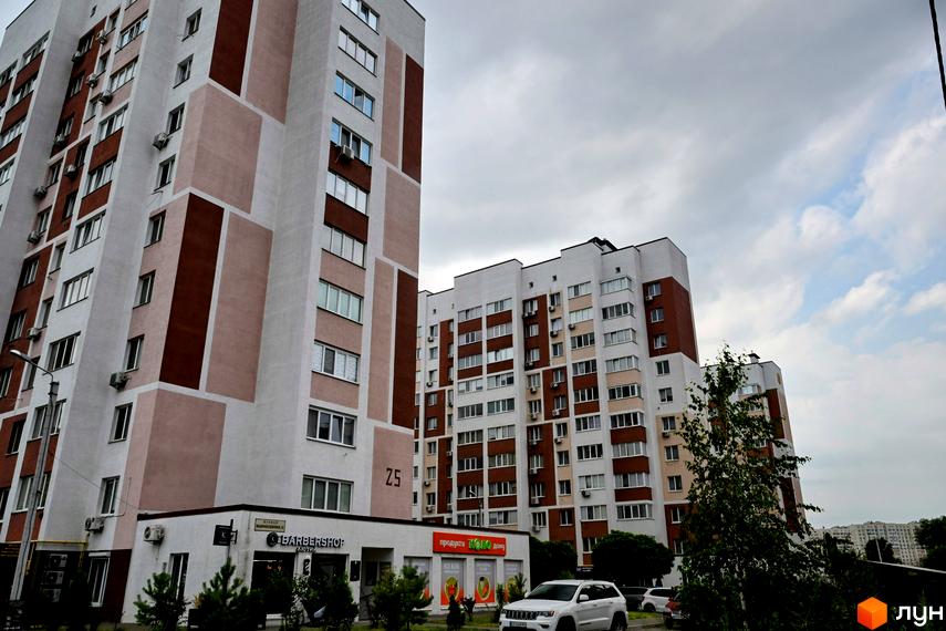 Житловий комплекс Сади Вишневі - це сучасна новобудова з біло-коричневим фасадом та великою кількістю вікон. Територія навколо будинку озеленена деревами та кущами.