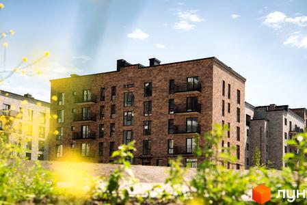 Новобудова WAWEL з цегляним фасадом та балконами на тлі блакитного неба. Навколо зелені насадження та квіти.