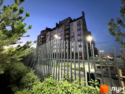 Житловий комплекс Park Residence з фасадом з сірих та бежевих панелей, вікнами та балконами, на фоні вечірнього неба. На прибудинковій території встановлено паркан та зелені насадження.
