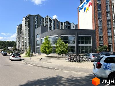 Зовнішній вигляд житлового комплексу Scandia з багаторівневими фасадами та панорамними вікнами. На прибудинковій території розташовані дерева та парковка з велосипедами.