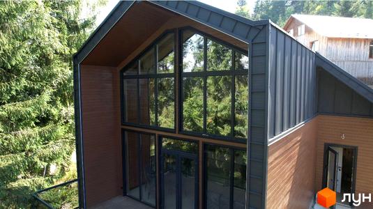 Зовнішній вигляд будинку КМ GORDO RESIDENCE з великими вікнами та дерев'яним фасадом, оточений хвойними деревами. На території видно іншу будівлю.