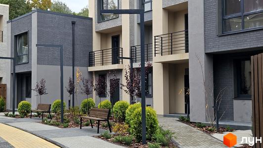 Зображення таунхаусів Sвій Dім 2 з сірого цегли, з балконами та лавками на прибудинковій території.